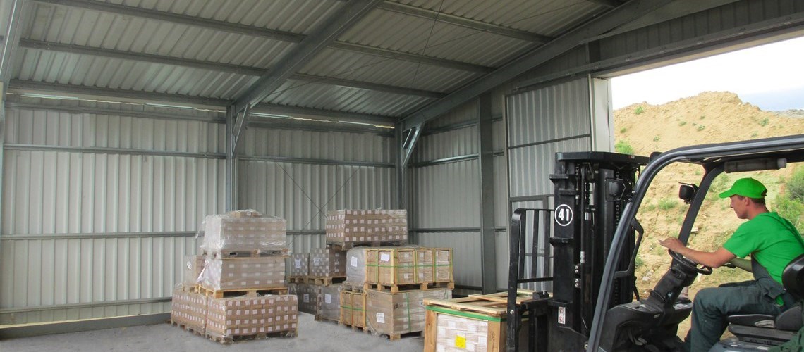 Vista interior de um hangar Delta utilizado como armazém, mostrando uma empilhadeira empilhar paletes